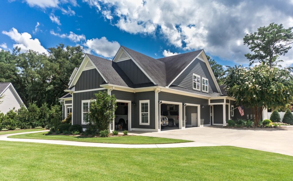 The side view of a large gray craftsman new construction house with a landscaped yard a three car garage and driveway drying time for oil-based paint